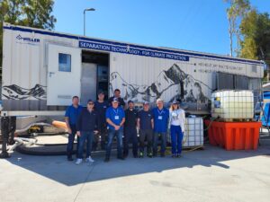 Eine Gruppe von zehn Personen steht vor einem großen weißen mobilen Gerät mit der Aufschrift Separation Technology - For Climate Protection. Das Fahrzeug ist mit Berggrafiken versehen und von Industrieanlagen umgeben.